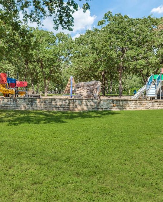 An outdoor playground surrounded by green grass and lush trees.